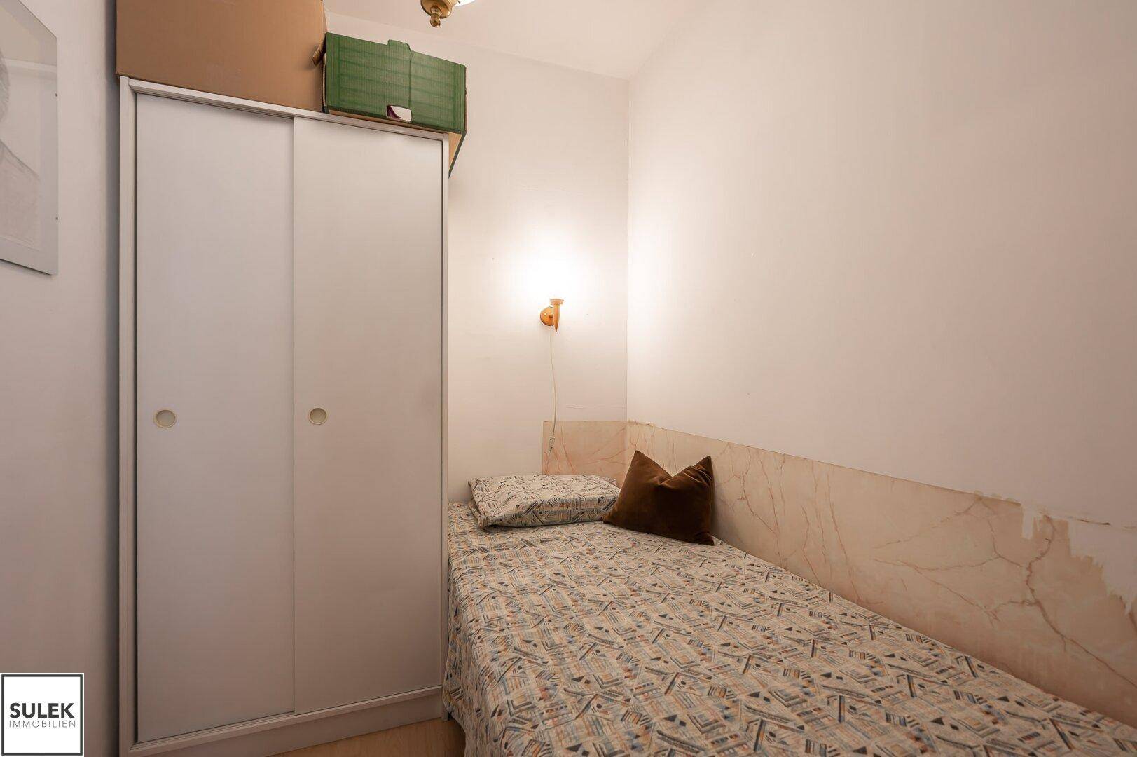 Kleines Schlafzimmer mit Einzelbett und weißem Kleiderschrank.