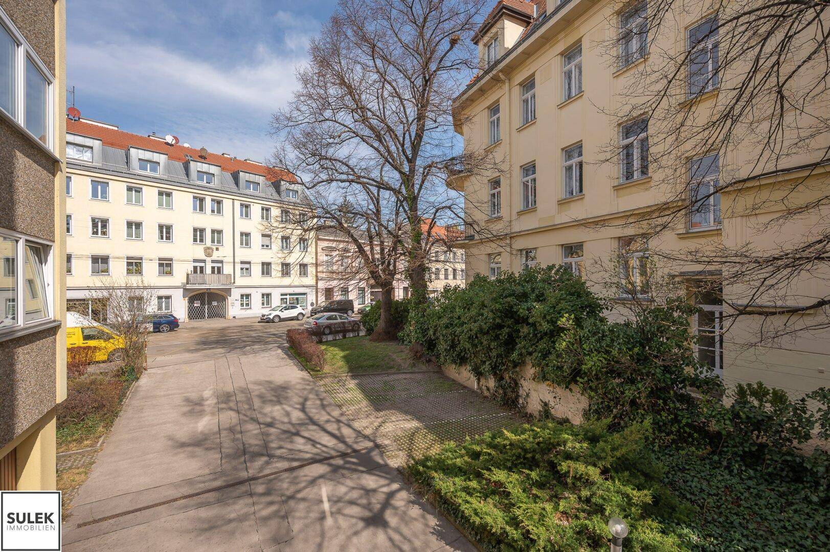 Innenhof mit Parkplätzen und Bäumen, umgeben von Wohngebäuden.