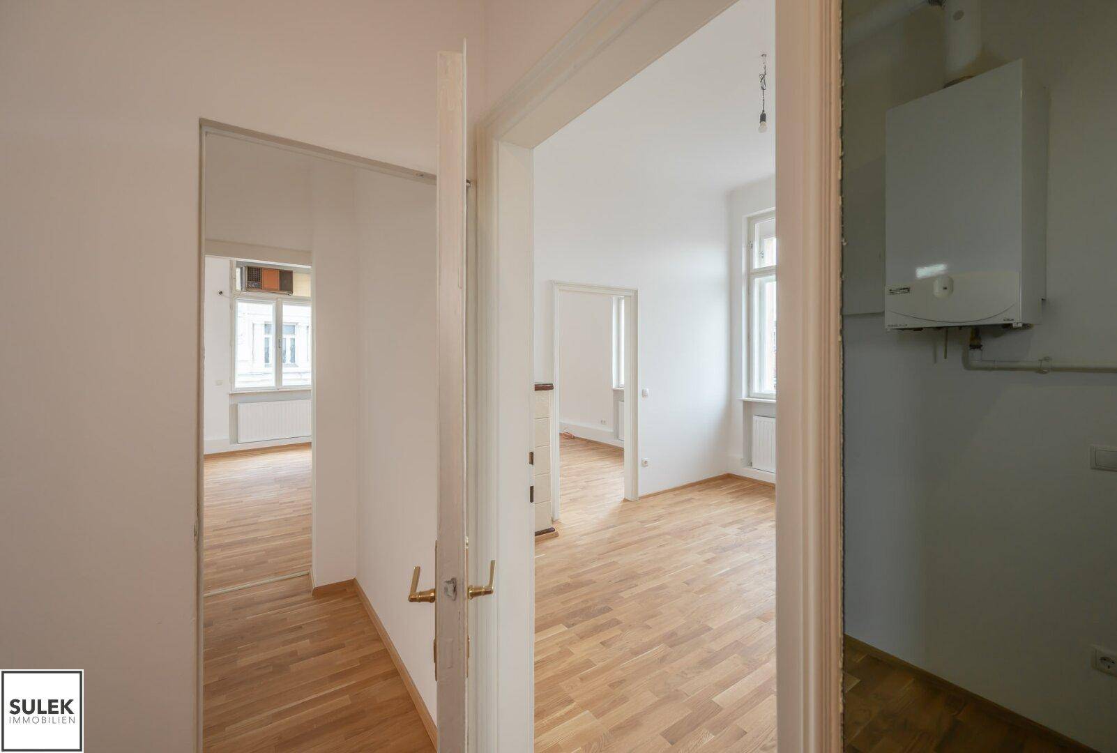 Blick durch offene Türen in mehrere helle Räume mit durchgehendem Holzboden und weißen Wänden.