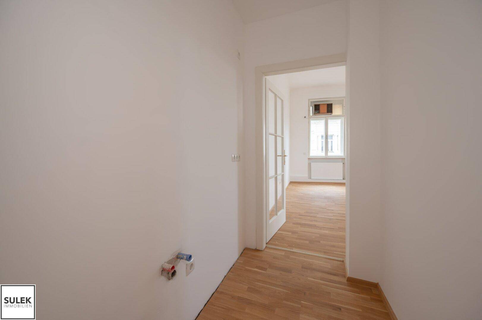 Heller Flur mit Holzboden und offenem Durchgang zu einem weiteren Zimmer mit viel Tageslicht.