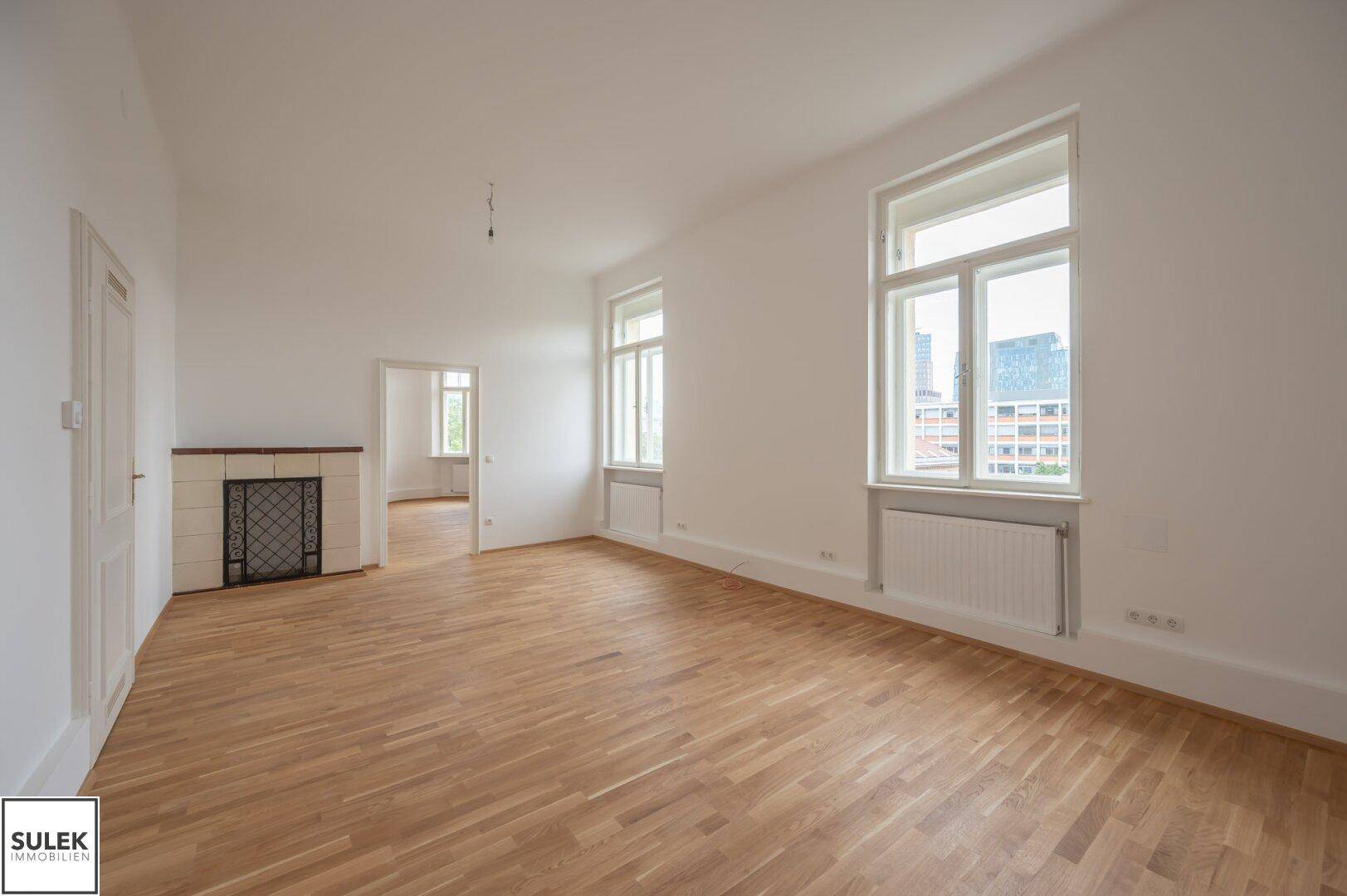 Heller Wohnraum mit Parkettboden, großen Fenstern und einem dekorativen Kachelofen.