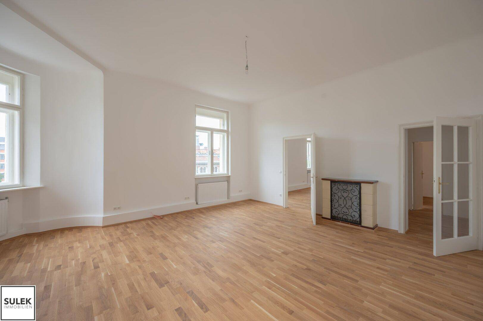 Großer, heller Raum mit Holzboden, mehreren Fenstern und einem traditionellen Kachelofen.