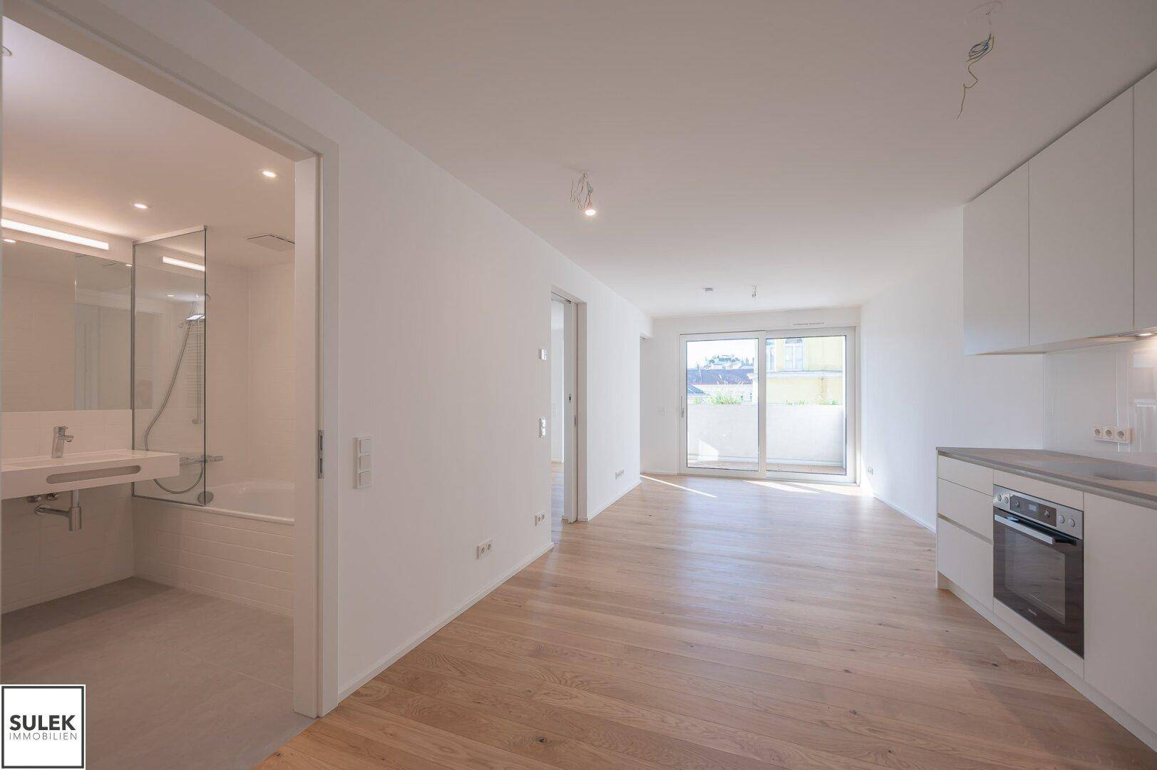 Offener Wohnbereich mit integrierter Küche, Holzboden und Zugang zum Balkon.