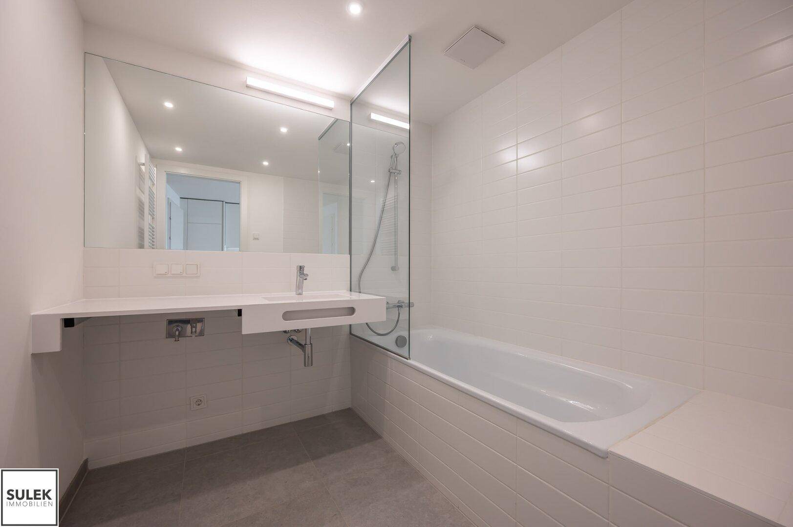 Modernes Badezimmer mit Badewanne, Einzelwaschbecken und großem Spiegel.