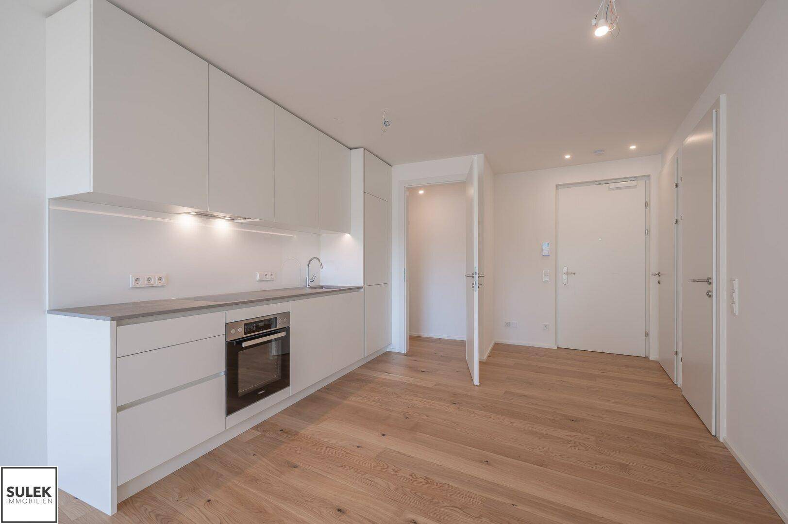 Moderne Einbauküche in Weiß mit integriertem Backofen und hellem Holzboden.