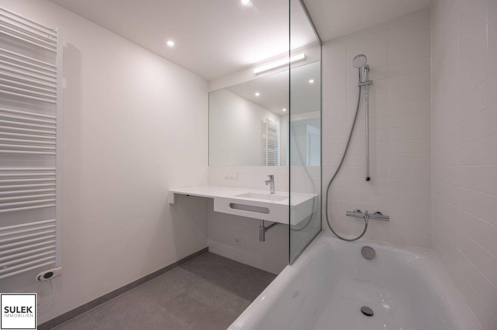 Helles Badezimmer mit Badewanne, Einzelwaschbecken und beheiztem Handtuchhalter.