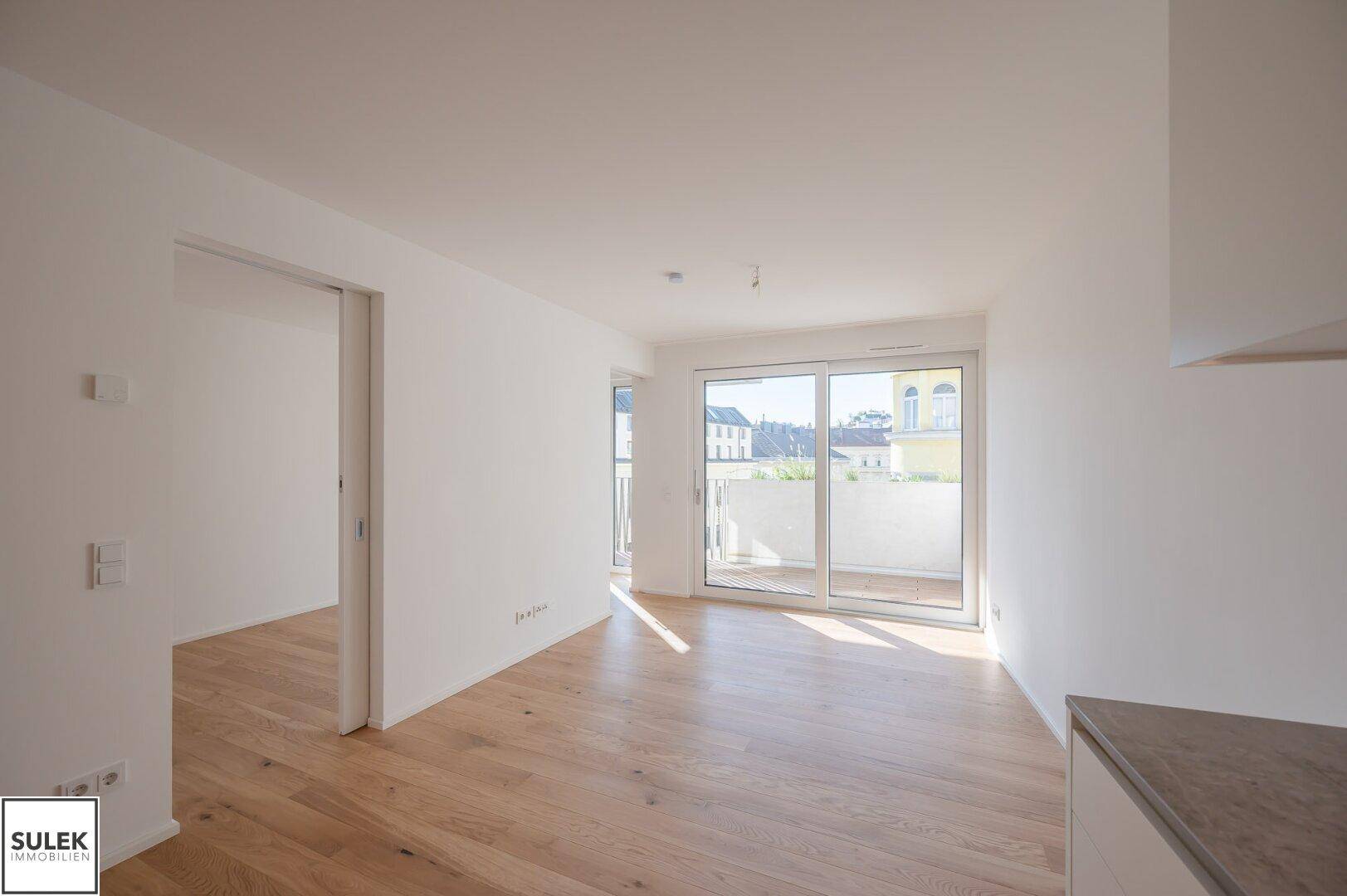 Offener Wohnbereich mit Holzboden und großzügigem Zugang zu einem sonnigen Balkon.