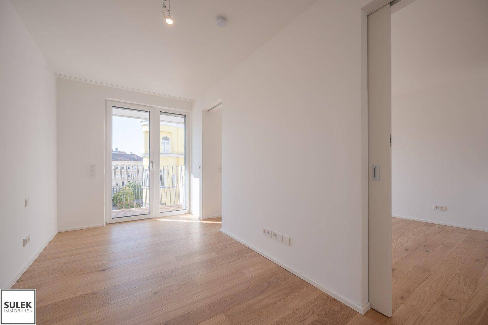 Helles Zimmer mit Holzboden und Balkonzugang, bietet einen Blick auf die Stadt.