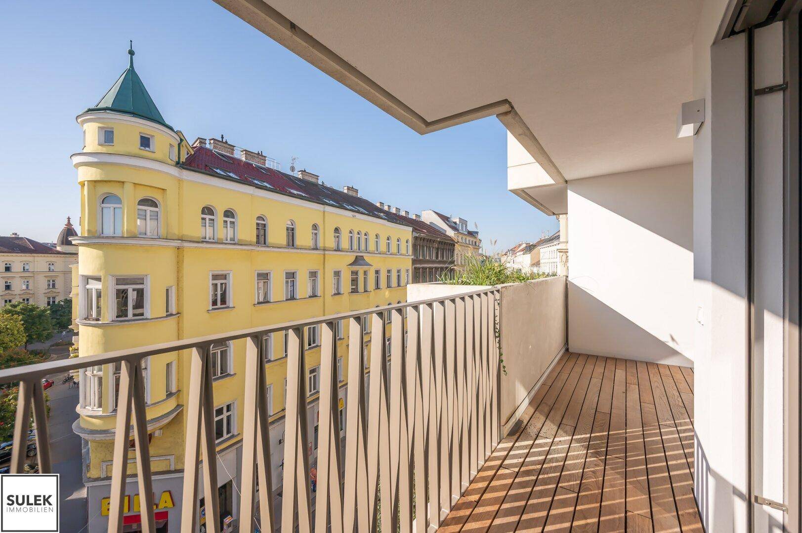 Geräumiger Balkon mit Holzboden und Blick auf ein charmantes historisches Gebäude.