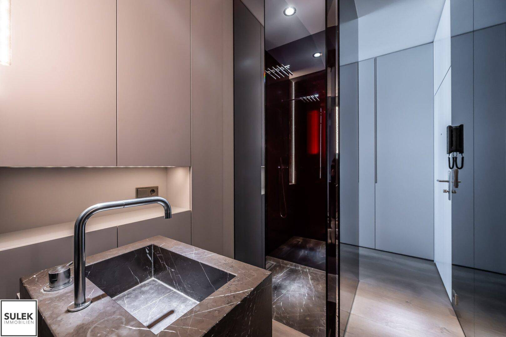 Luxuriöses Badezimmer mit dunklem Marmorwaschbecken und einer modernen Duschkabine mit Regendusche.