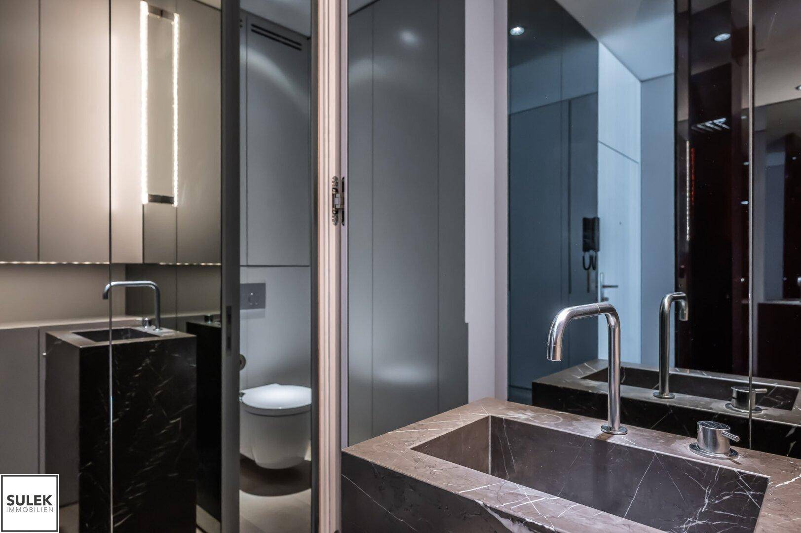 Stilvolles Badezimmer mit dunklem Marmorwaschbecken und Spiegeln, die den Raum optisch vergrößern.