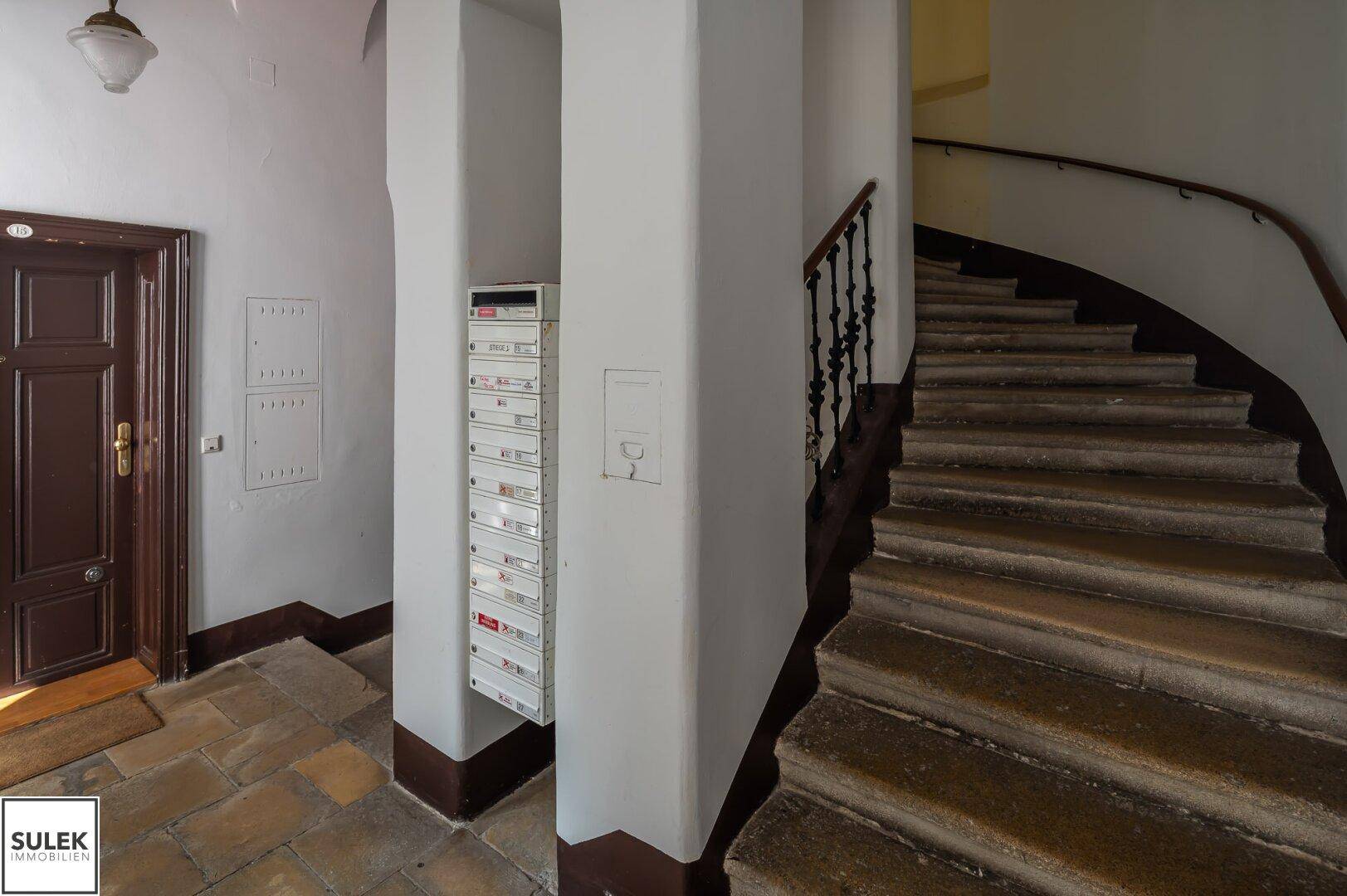 Eingangsbereich eines Altbaus mit historischer Treppe, Briefkästen und traditionellem Fliesenboden.