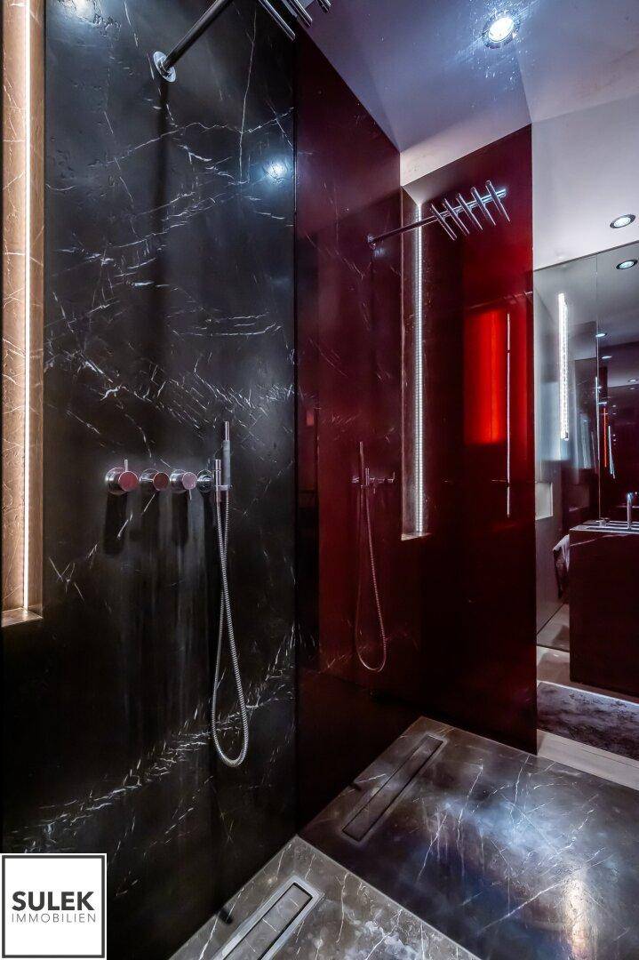 Elegante Duschkabine mit schwarzen Marmorfliesen, Regendusche und stilvoller Beleuchtung.