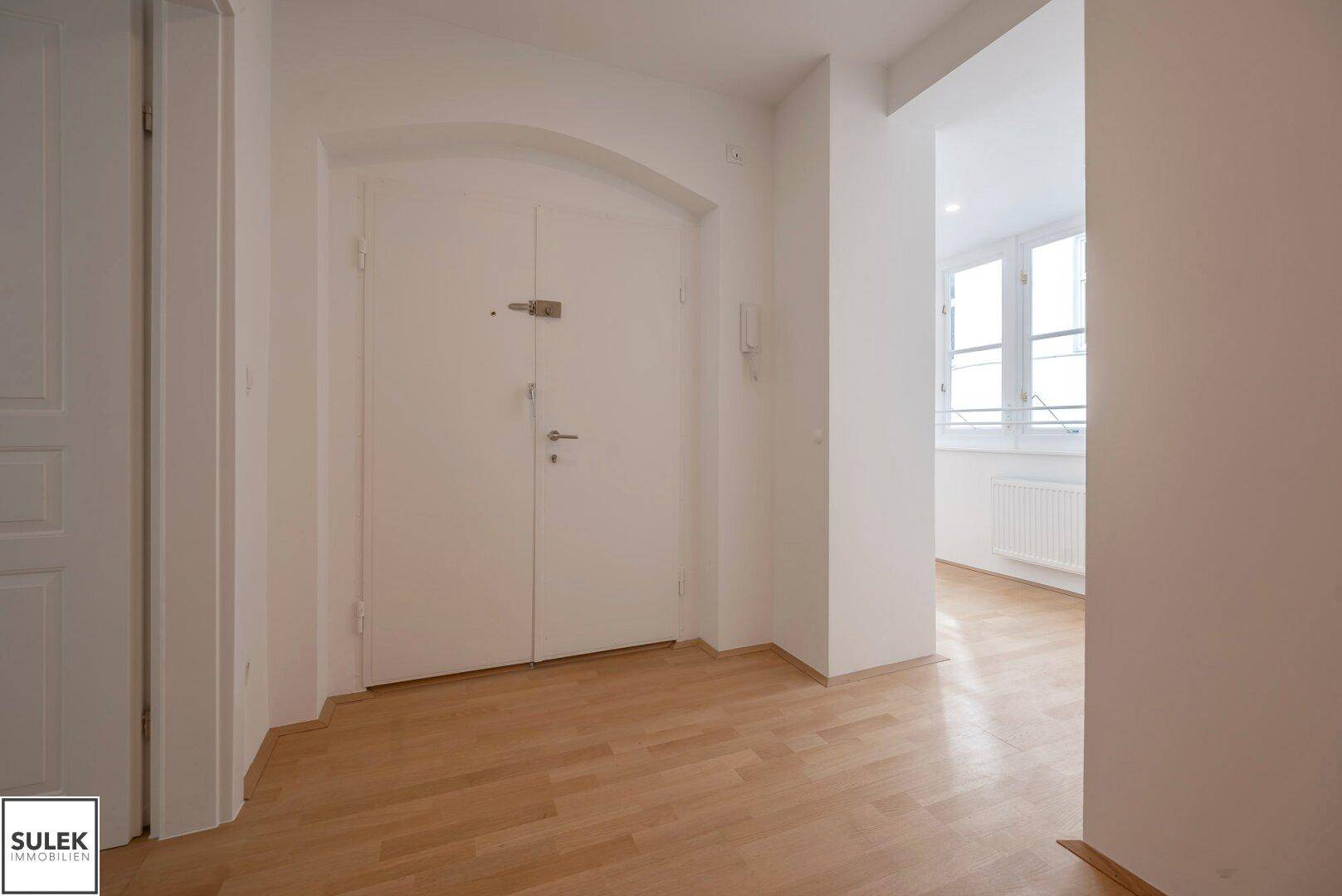 Heller Eingangsbereich mit Holzboden und weißer Doppeltür, die zu den Wohnräumen führt.