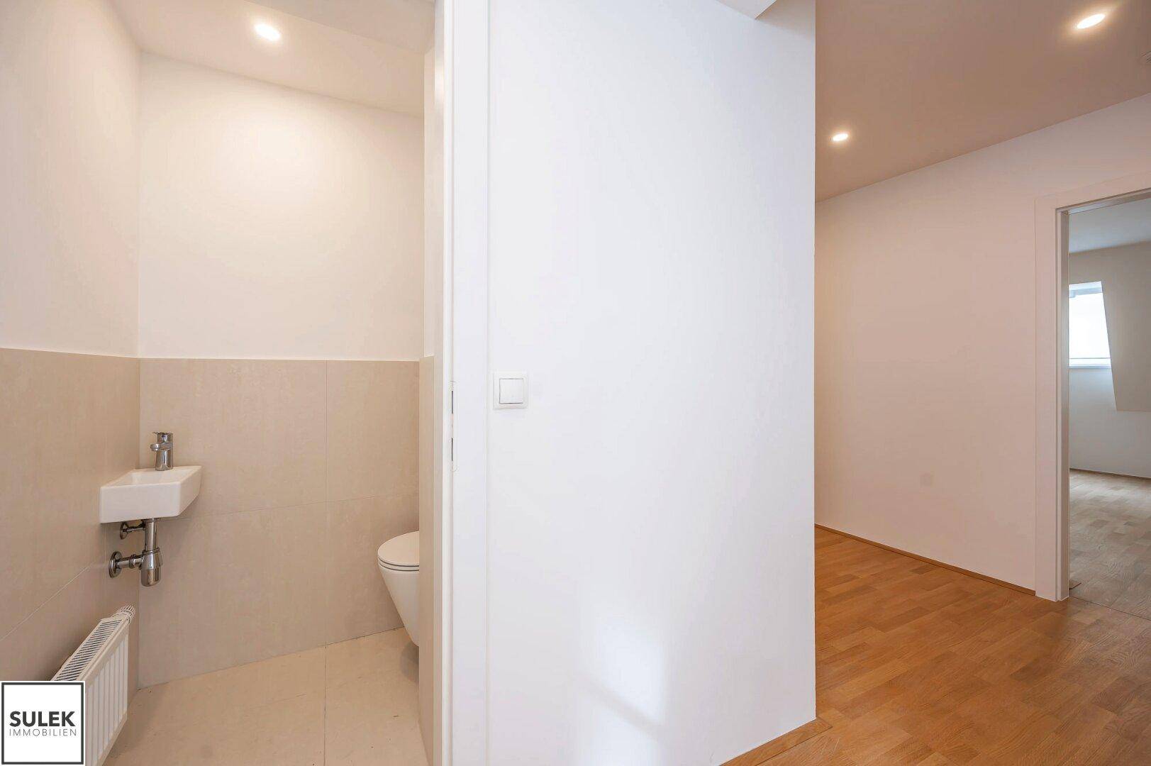 Modernes Gäste-WC mit Wand-WC, kleinem Waschbecken und hellen Fliesen.