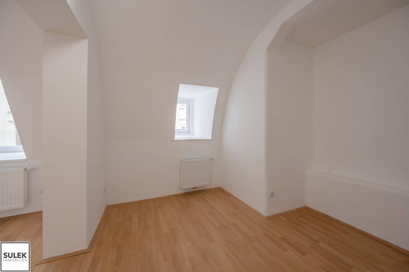Helles Zimmer mit Parkettboden, gewölbter Decke und einem Fenster, das viel Licht spendet.