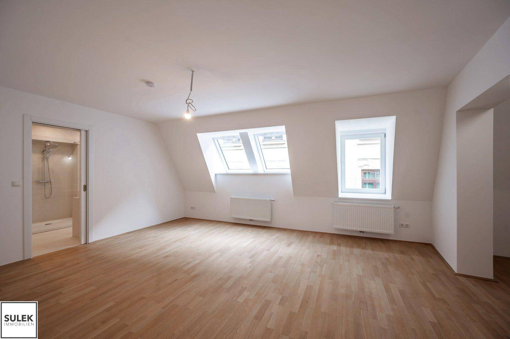 Geräumiges Zimmer mit Dachschrägen, Parkettboden und Zugang zu einem modernen Badezimmer.