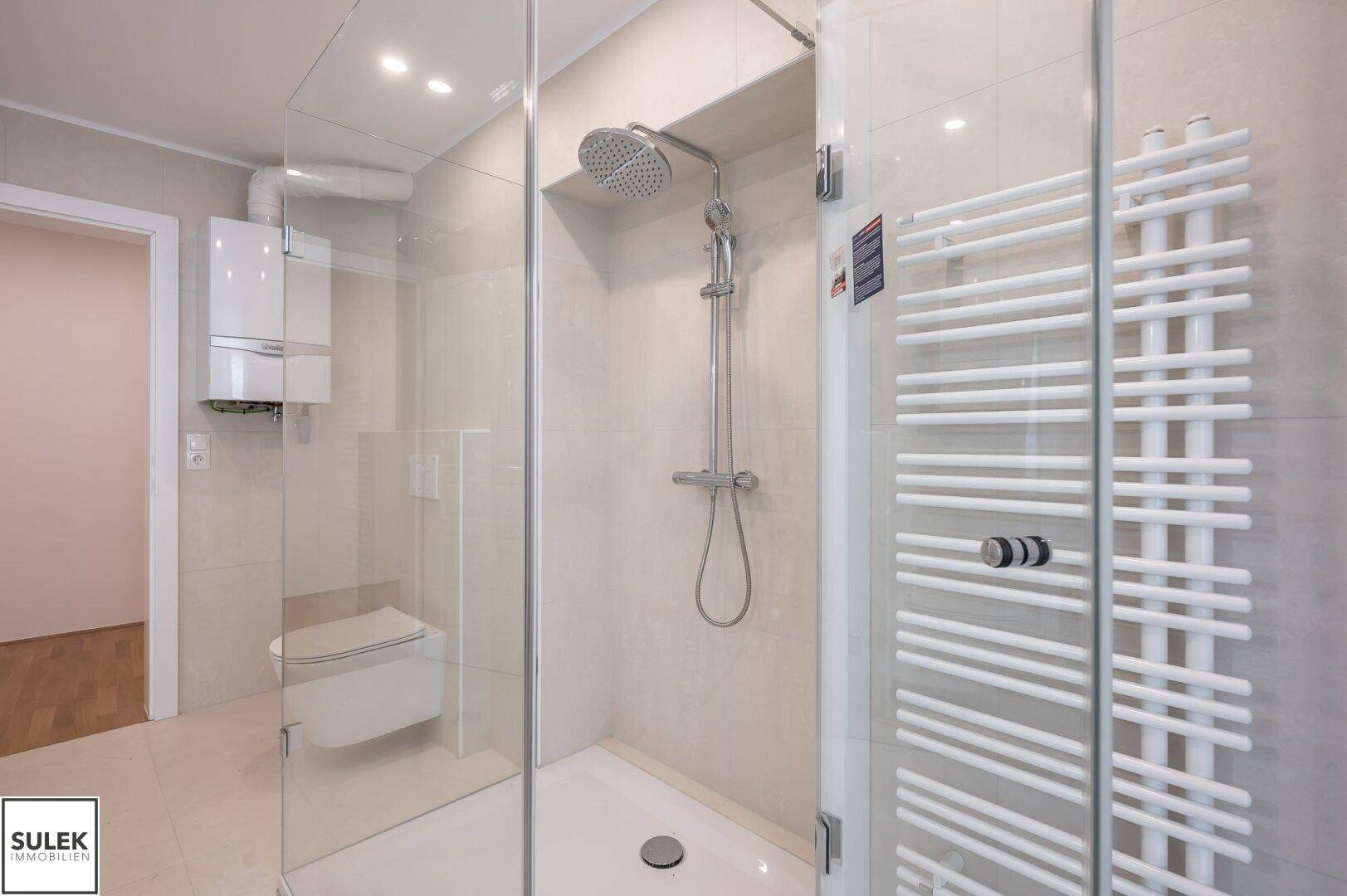 Moderne begehbare Dusche mit Regenduschkopf und Handtuchheizkörper in einem hell gefliesten Badezimmer.