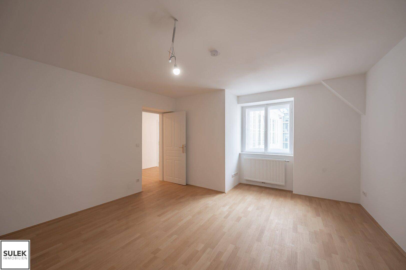 Helles Zimmer mit Parkettboden und Fenster, das viel Tageslicht in den Raum lässt.