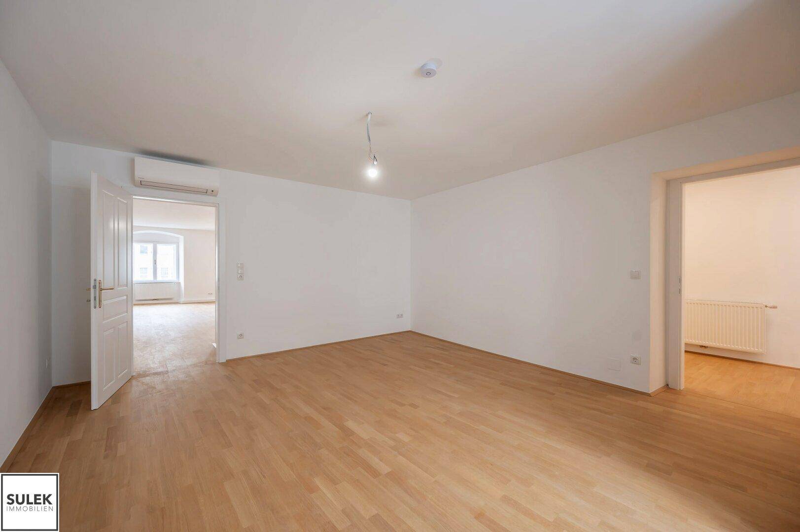 Geräumiges, helles Zimmer mit Parkettboden und Klimaanlage, bereit zur individuellen Einrichtung.
