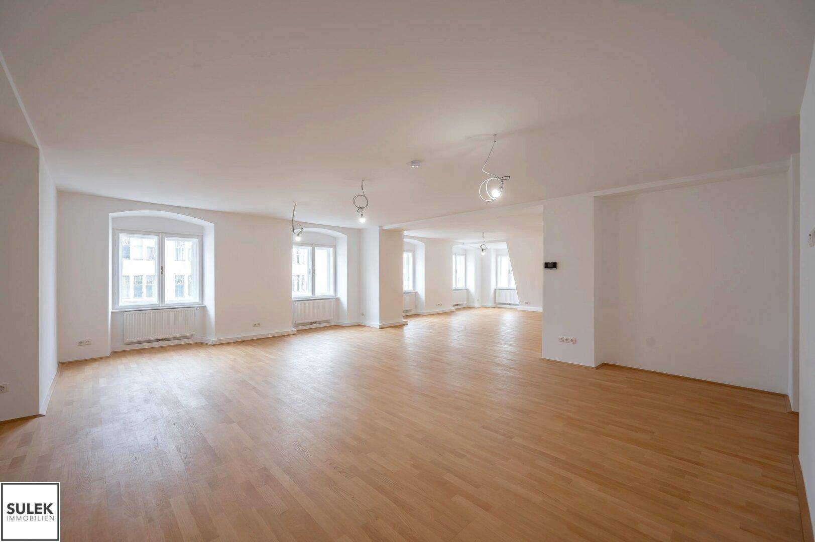 Geräumiger, heller Wohnbereich mit Parkettboden und mehreren Fenstern, bereit zur individuellen Gestaltung.