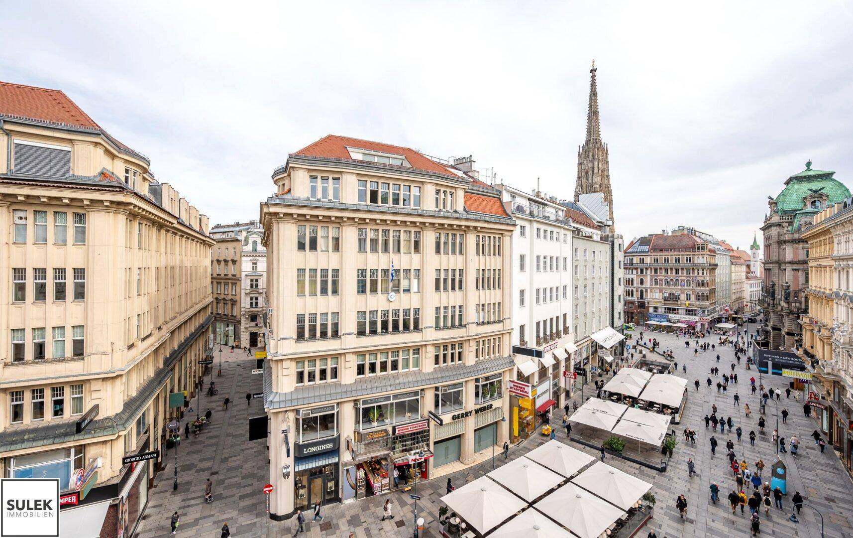 Panoramablick über eine belebte Wiener Einkaufsstraße mit historischen Gebäuden und Stephansdom im Hintergrund.