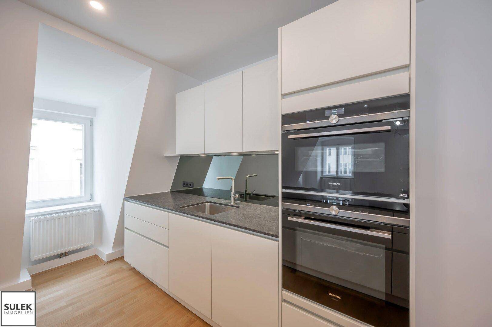 Moderne Einbauküche mit integrierten Siemens-Geräten, dunkler Arbeitsplatte und Parkettboden.