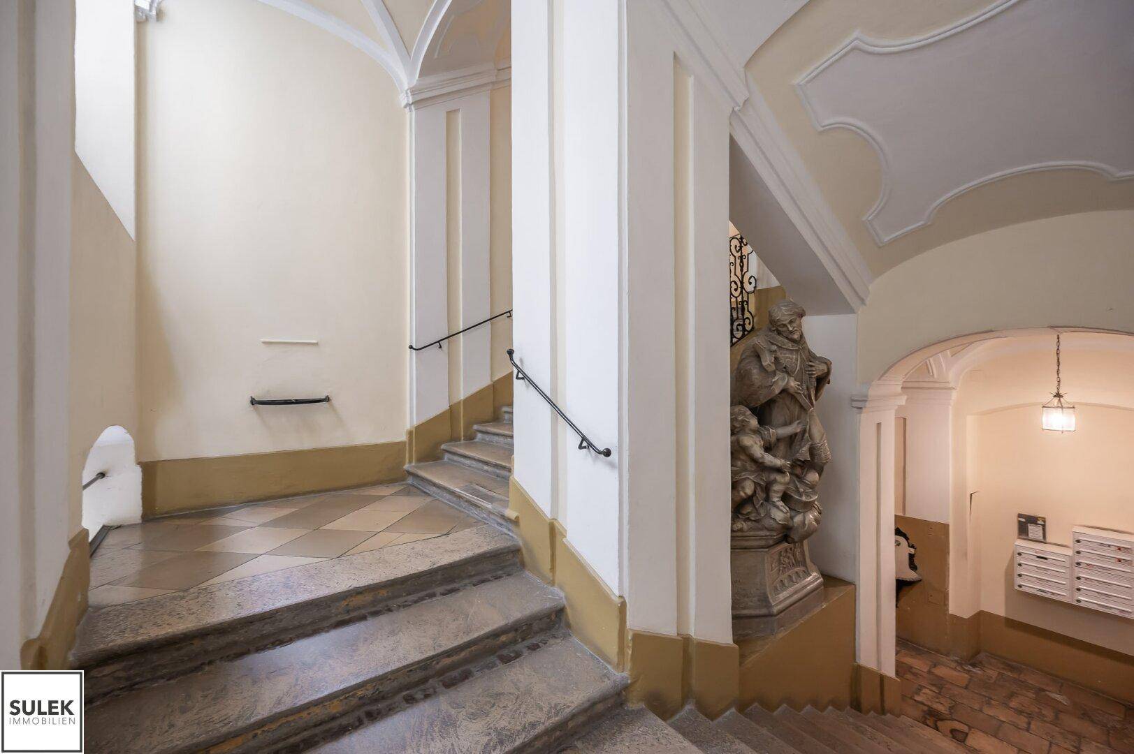 Elegantes Treppenhaus mit Steinstufen, einer Statue und historischen Details.