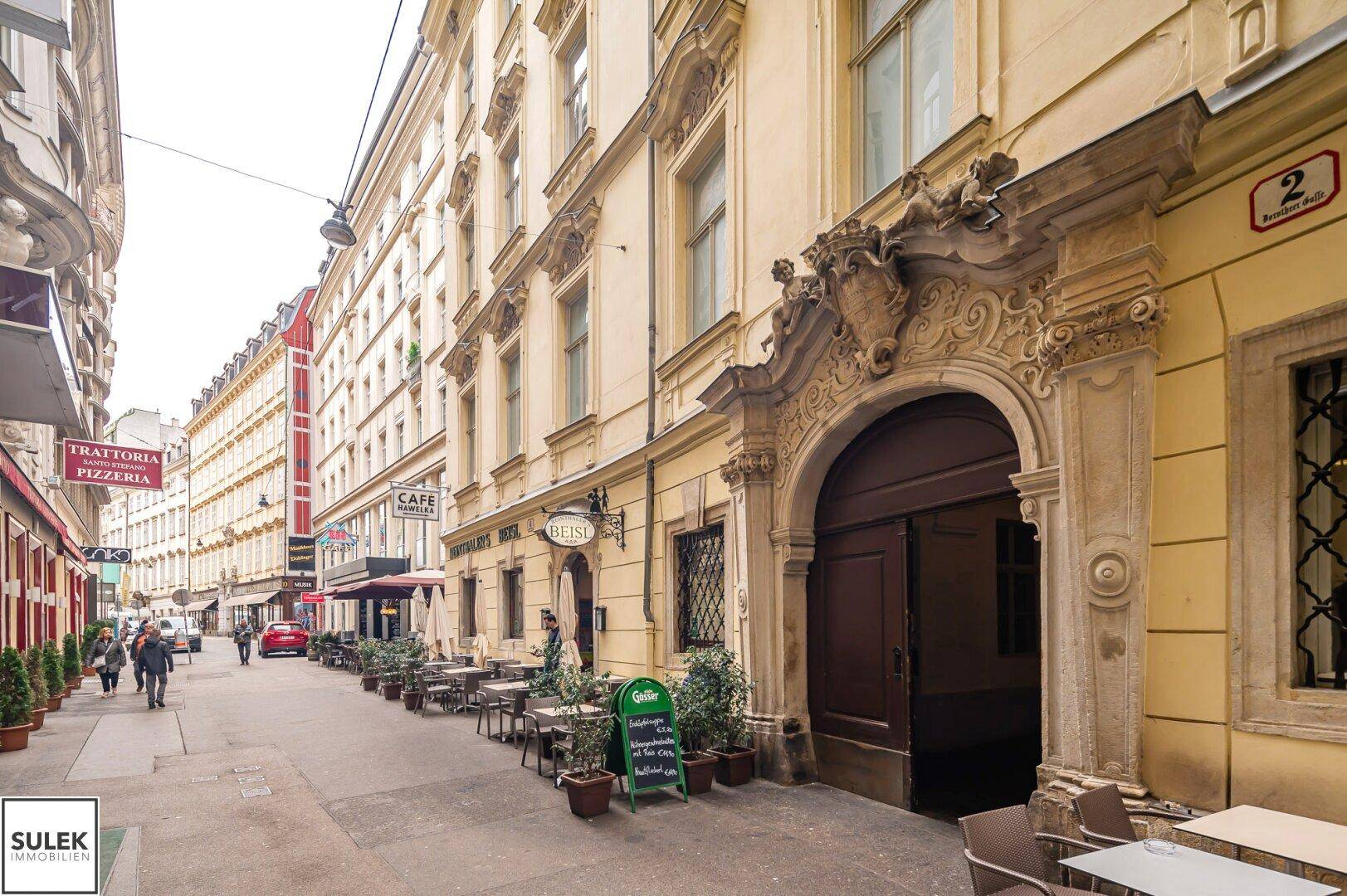 Historische Straßenansicht mit einem charmanten Gebäude, Außengastronomie und Passanten.