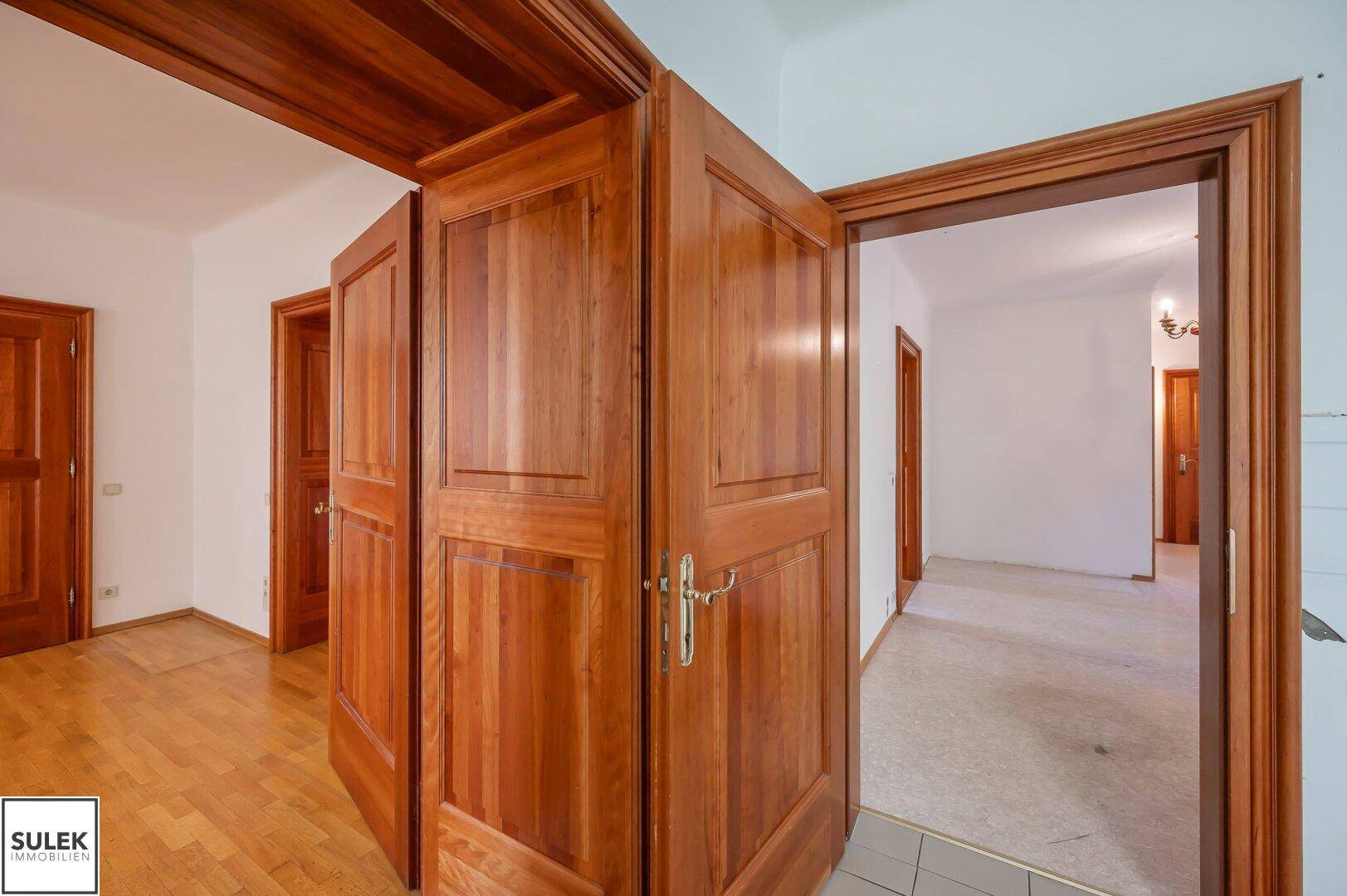 Geräumiger Flur mit mehreren klassischen Holztüren und hellem Holzfußboden, der verschiedene Bereiche verbindet.