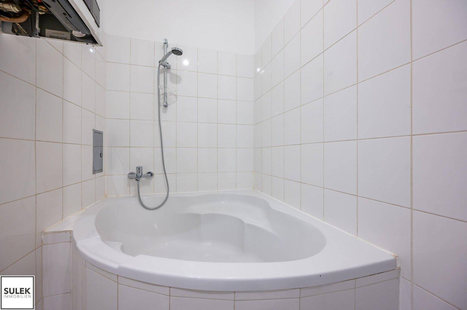 Eckbadewanne mit Duschfunktion in einem hell gefliesten Badezimmer.