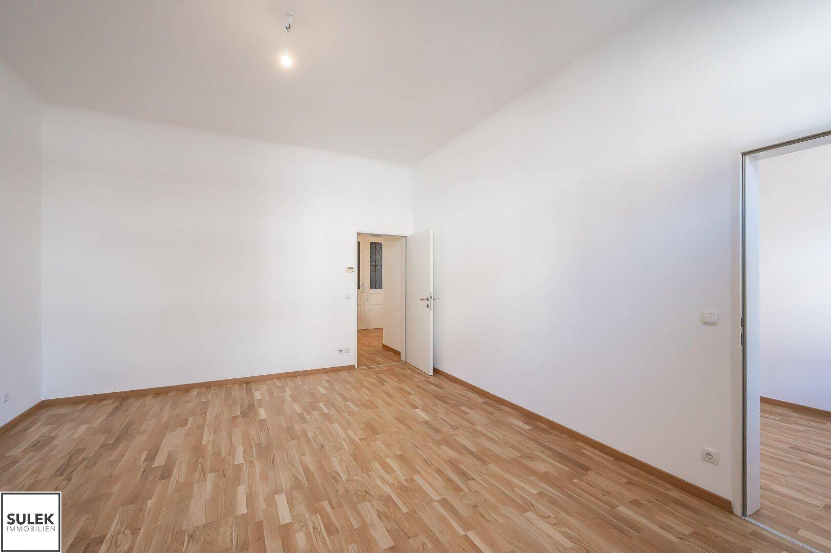 Helles Zimmer mit Parkettboden und weißen Wänden, bereit zur individuellen Gestaltung.