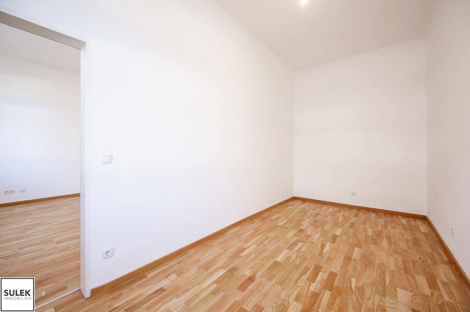 Leeres Zimmer mit Parkettboden und weißen Wänden, ideal als Schlaf- oder Arbeitszimmer.
