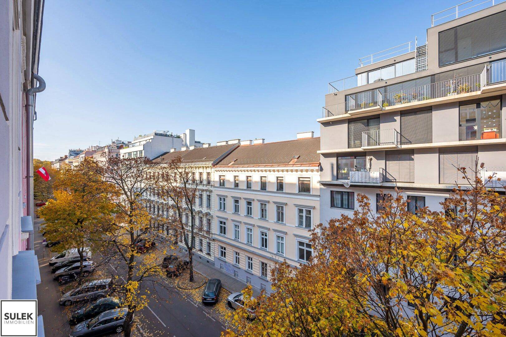 Blick auf eine belebte Straße mit herbstlichen Bäumen und umliegenden Gebäuden.
