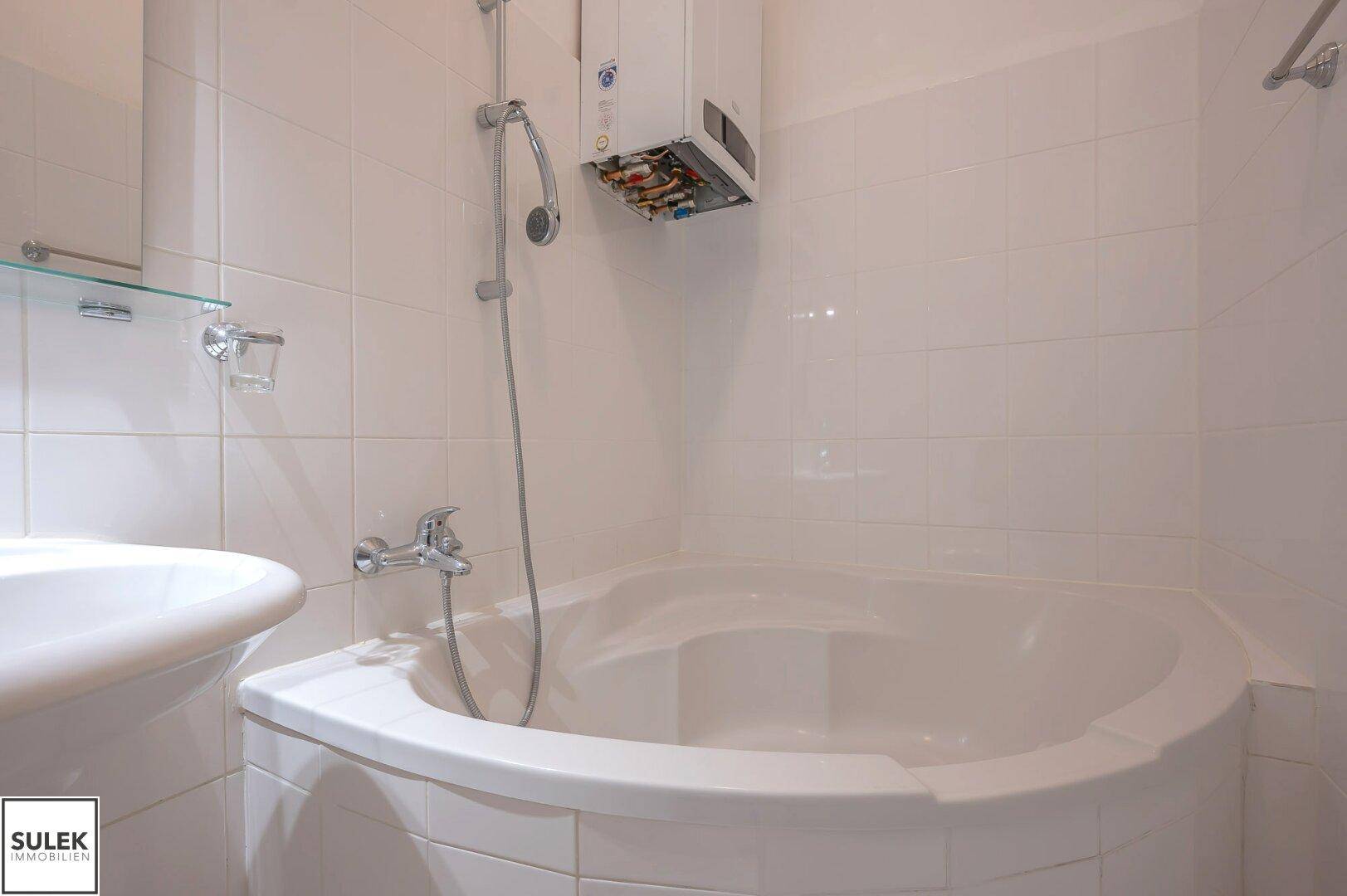 Eckbadewanne mit Duscharmatur und weißem Fliesenbelag, ideal für entspannende Bäder.