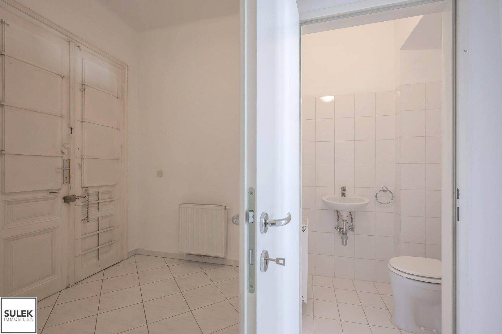 Separates WC mit Waschbecken und weißen Wand- und Bodenfliesen, funktional und sauber.