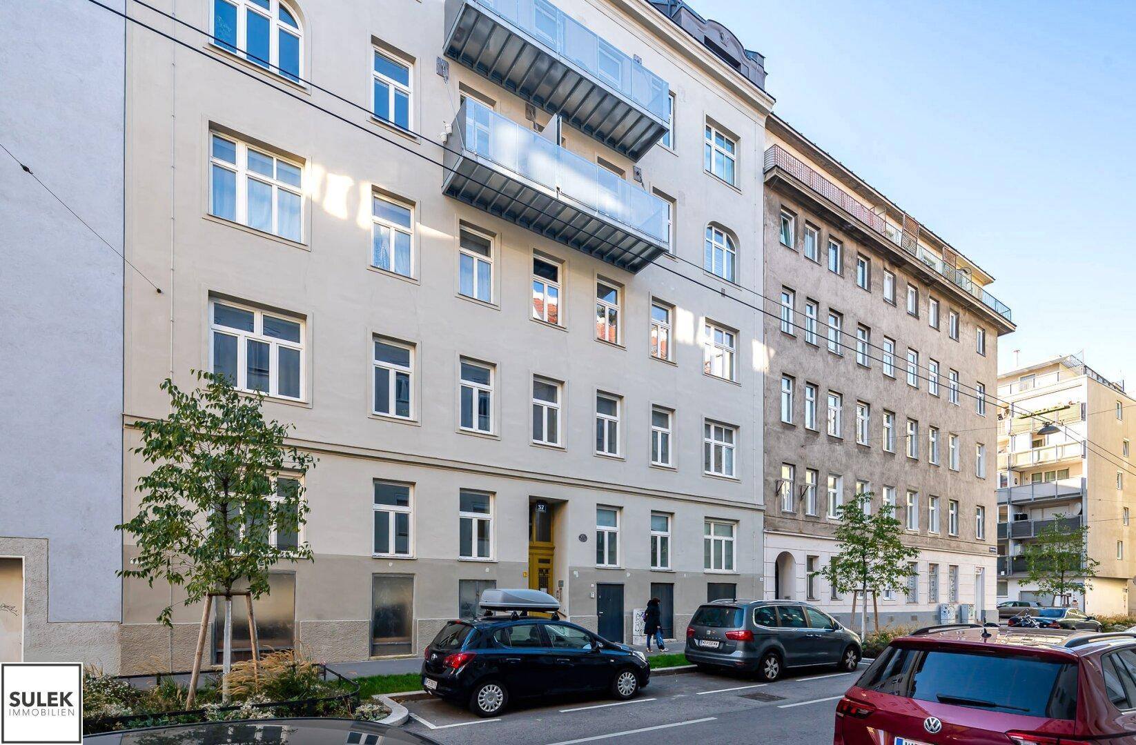 Fassade eines Mehrfamilienhauses mit vielen Fenstern und Balkonen an einem sonnigen Tag.