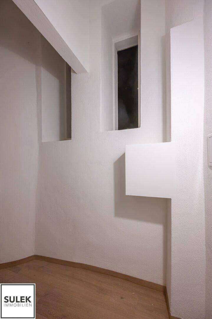 Heller, leerer Raum mit Holzboden und ungewöhnlicher Fenstergestaltung.