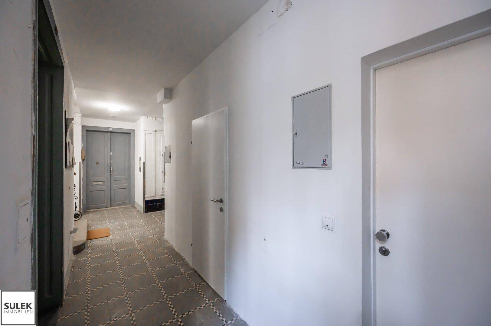 Langer Flur in einem Altbau mit gemusterten Fliesen und mehreren Türen.