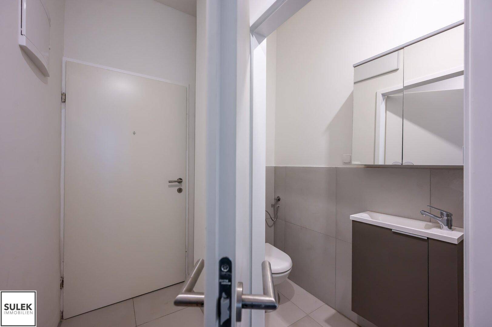 Heller Eingangsbereich mit weißer Tür und Blick in ein angrenzendes Badezimmer.