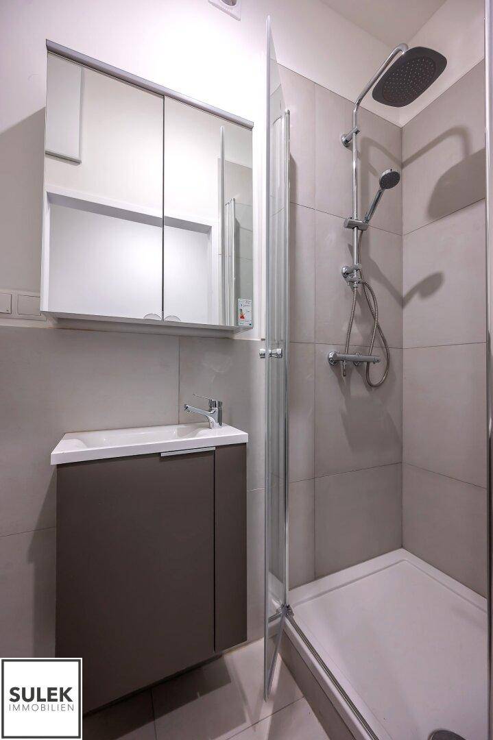 Modernes Badezimmer mit Duschkabine, Waschbeckenunterschrank und Spiegelschrank in neutralen Tönen.