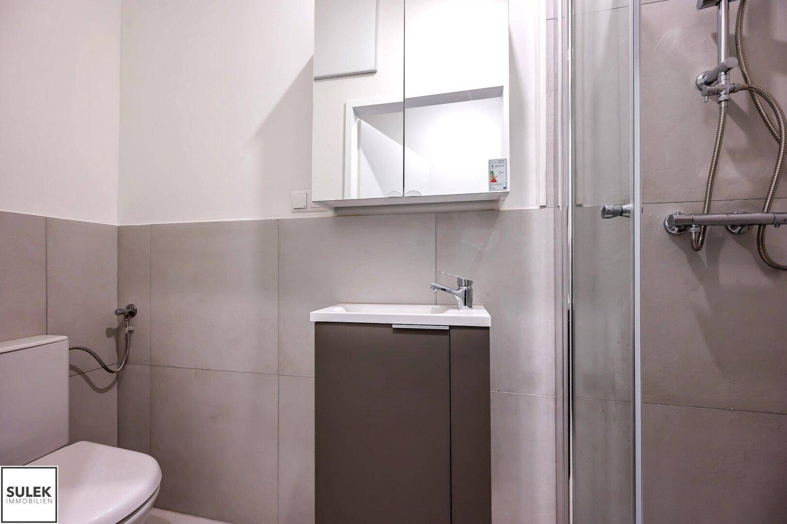 Kleines Badezimmer mit WC, Waschbeckenunterschrank und Duschkabine in neutralen Farben.