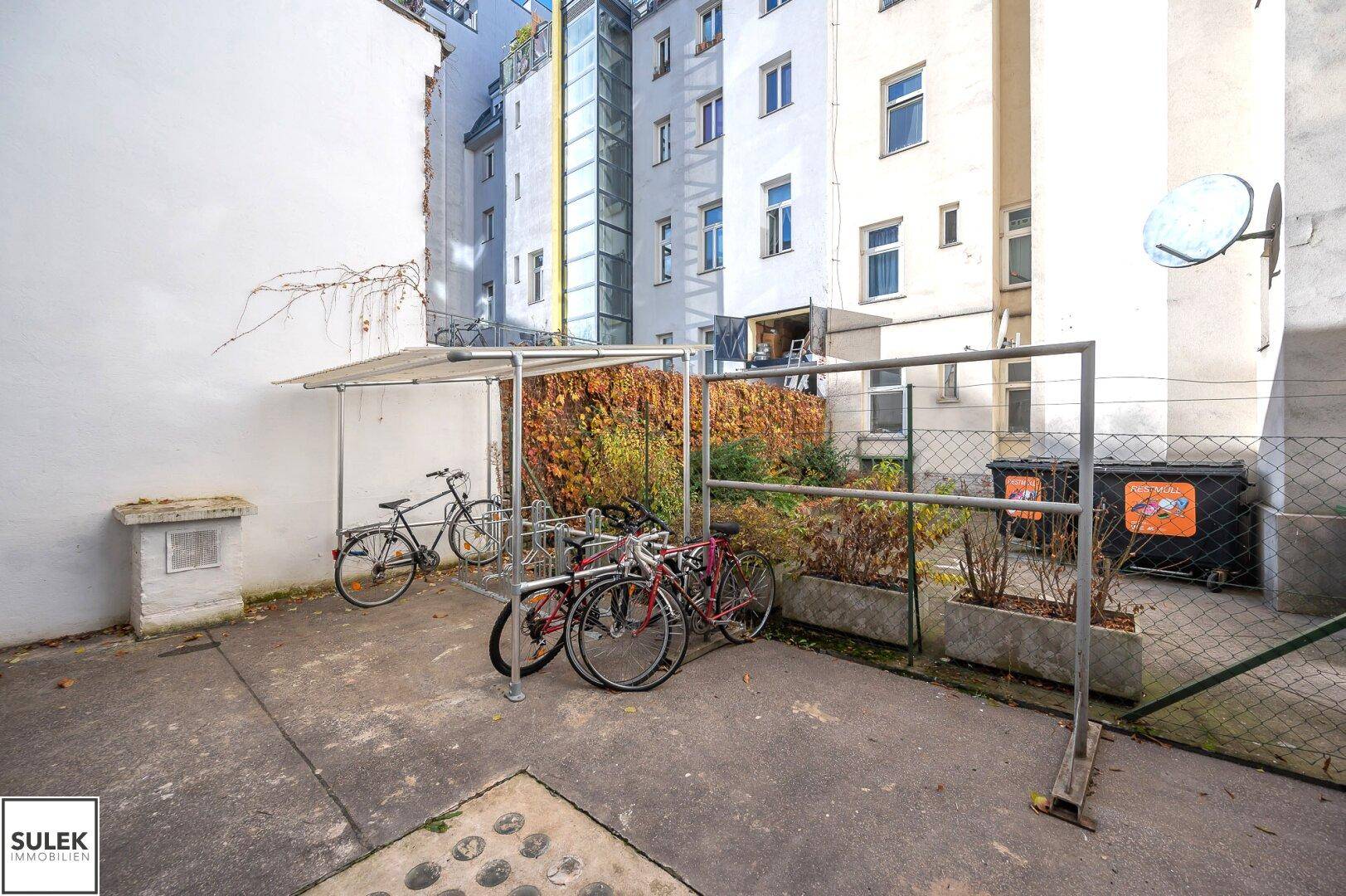 Innenhof mit Fahrradabstellplatz und Mülltonnen, umgeben von Gebäuden.