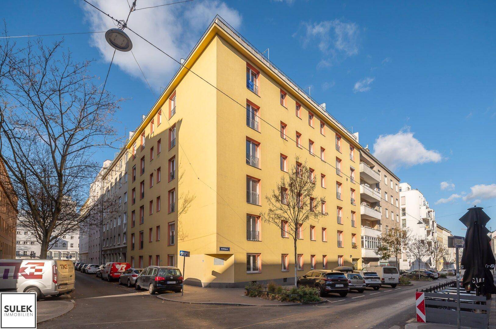 Eckgebäude mit gelber Fassade und vielen Fenstern an einer städtischen Kreuzung.
