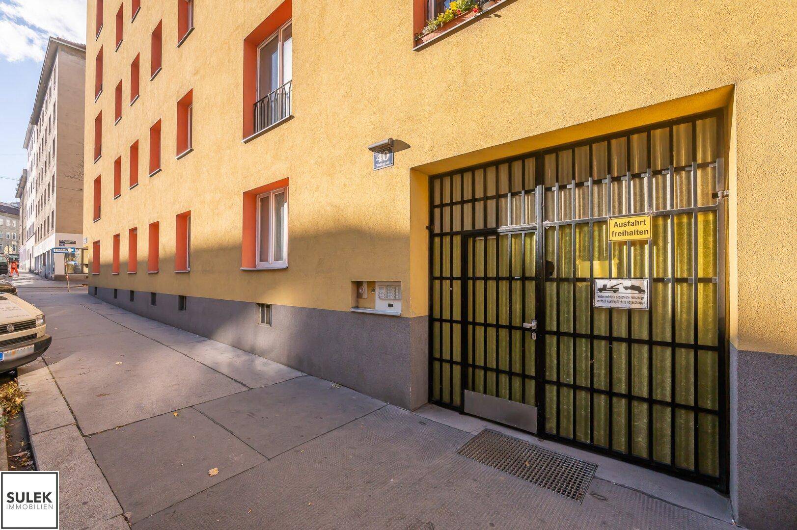 Garageneinfahrt mit Metalltor an der Fassade eines gelben Wohngebäudes an der Straße.
