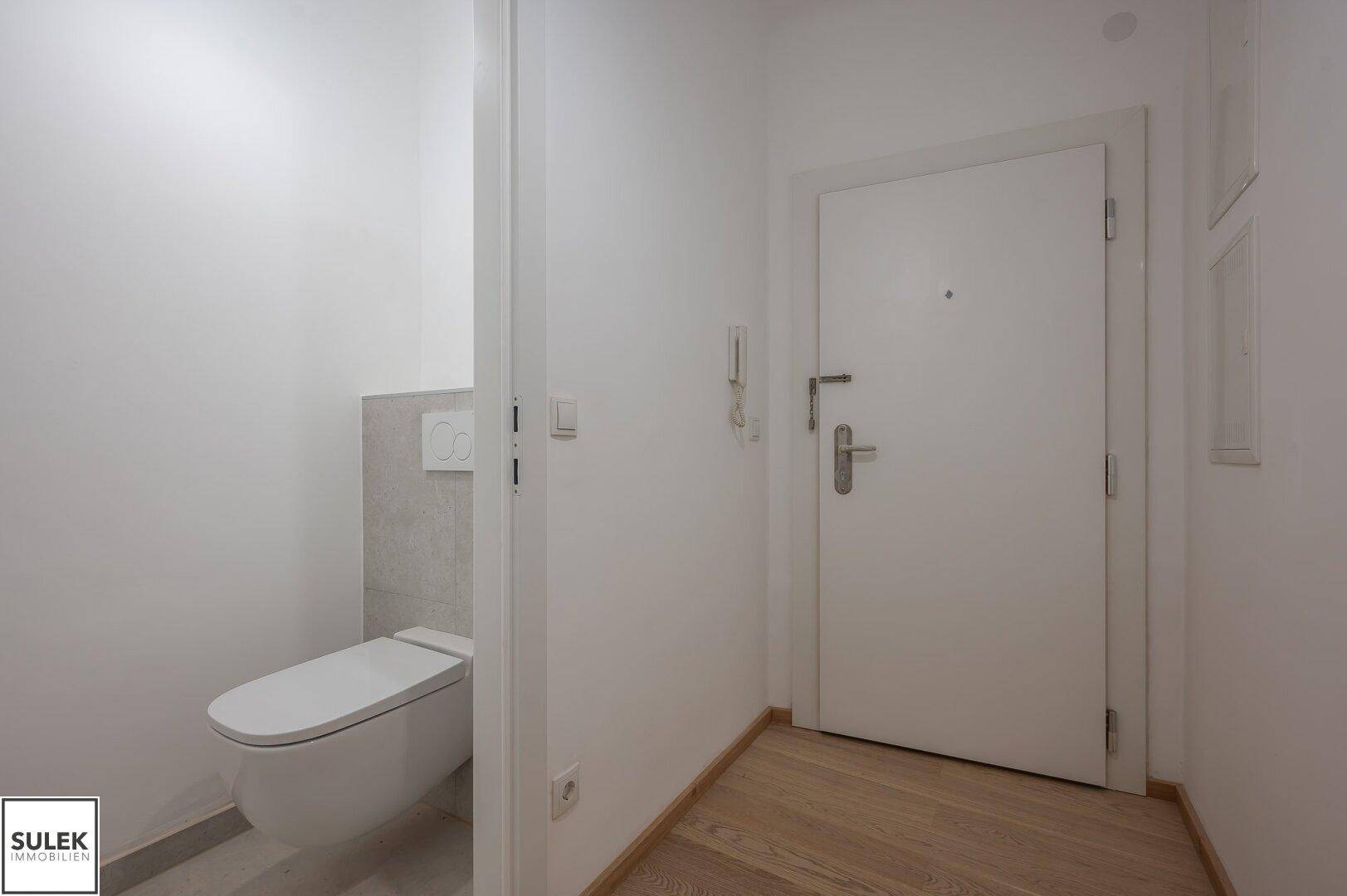 Separates Gäste-WC mit wandhängender Toilette und hellem Holzboden im Eingangsbereich der Wohnung.