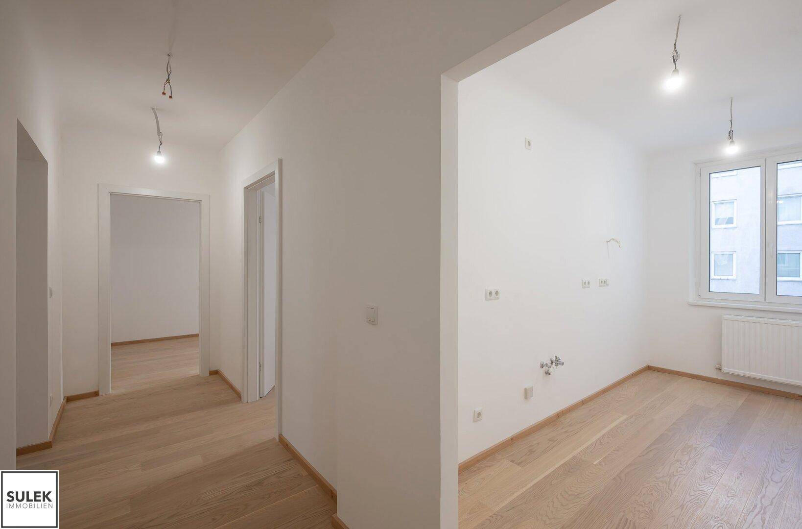 Geräumiger Flur mit hellem Holzboden und Blick in ein weiteres Zimmer mit Fenster.