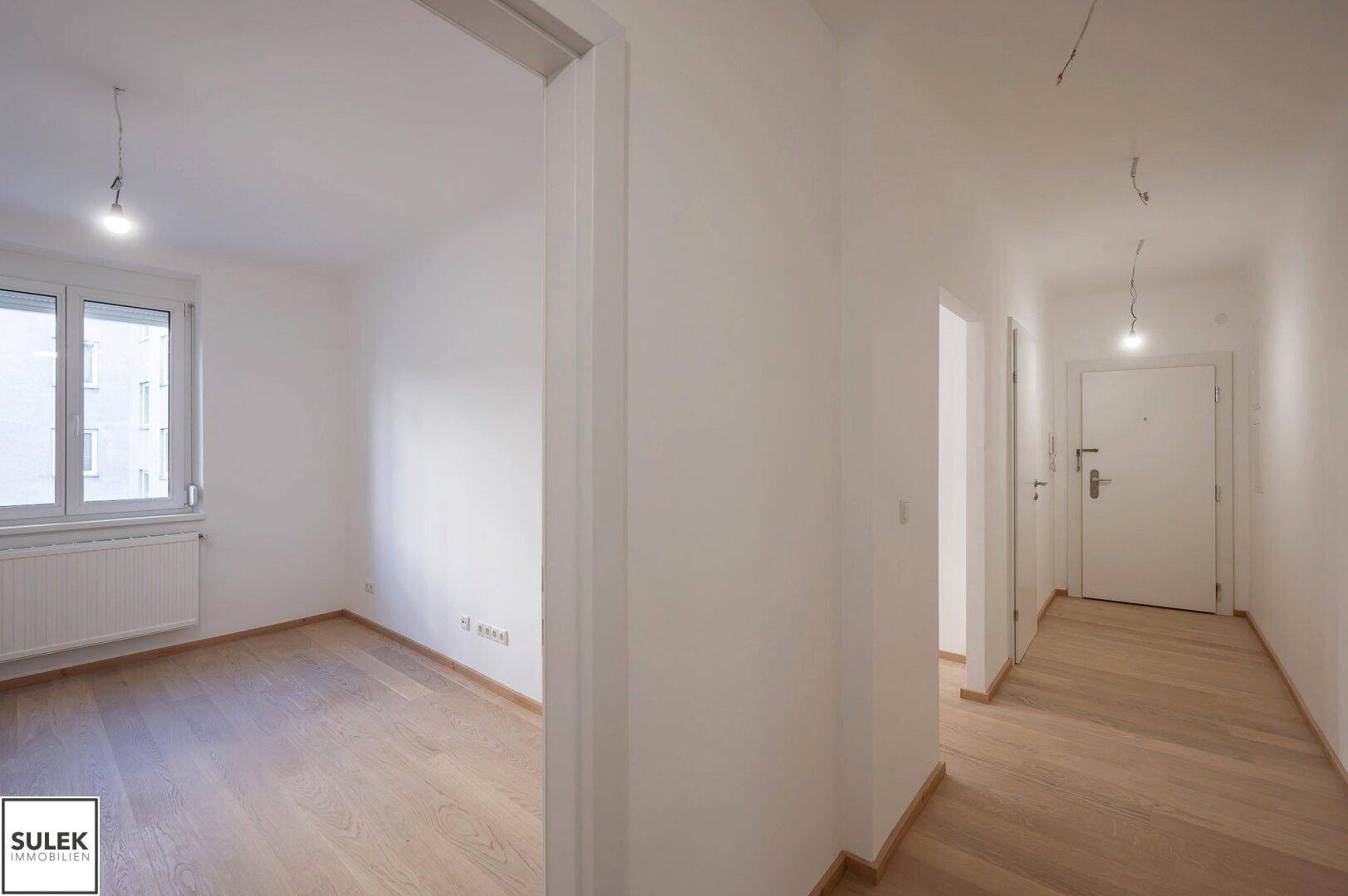 Heller Flur mit Holzboden, der zu einem weiteren Zimmer und dem Eingangsbereich führt.