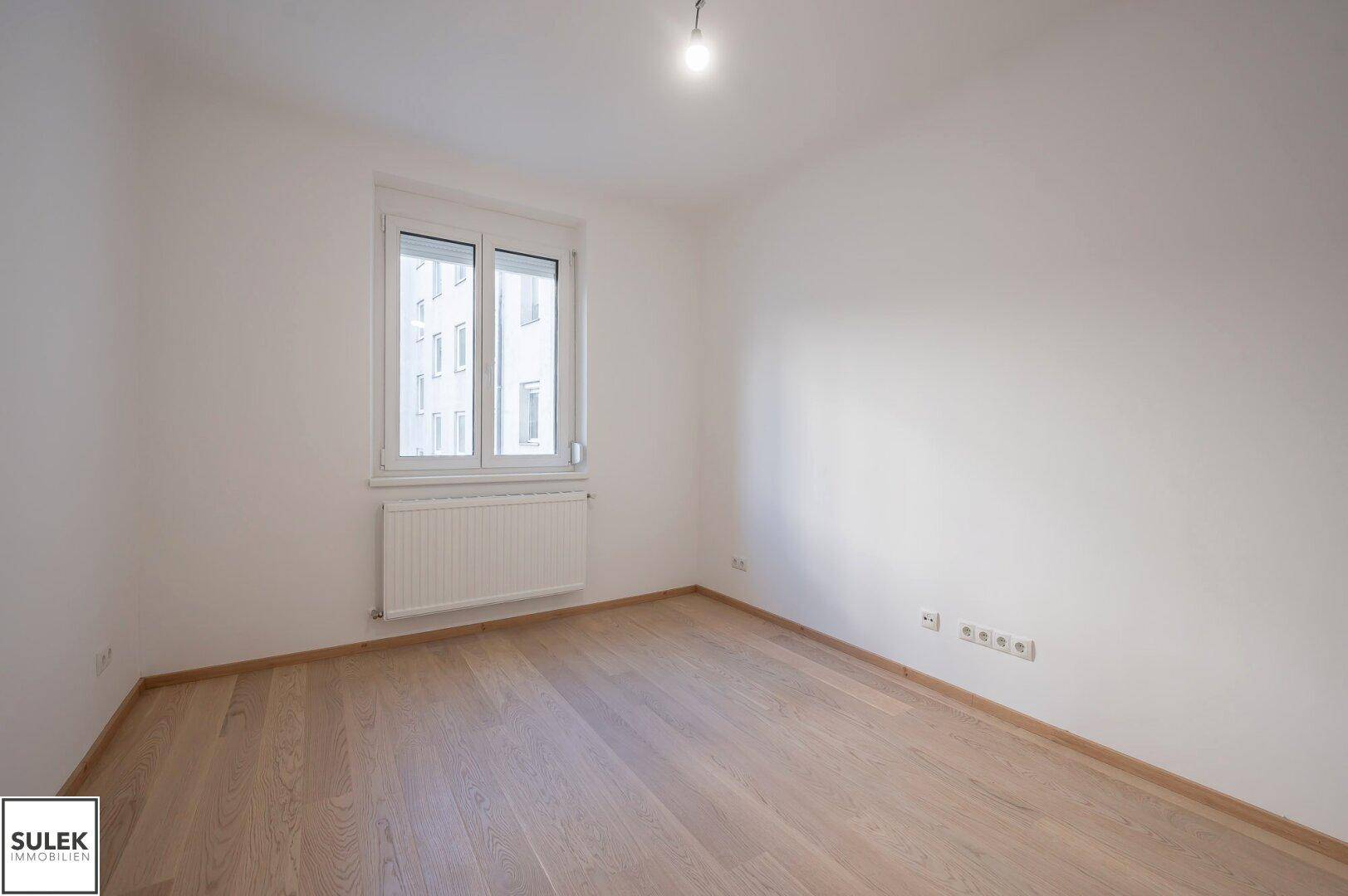Leeres Schlafzimmer mit hellem Holzboden und großem Fenster, bereit zur individuellen Gestaltung.