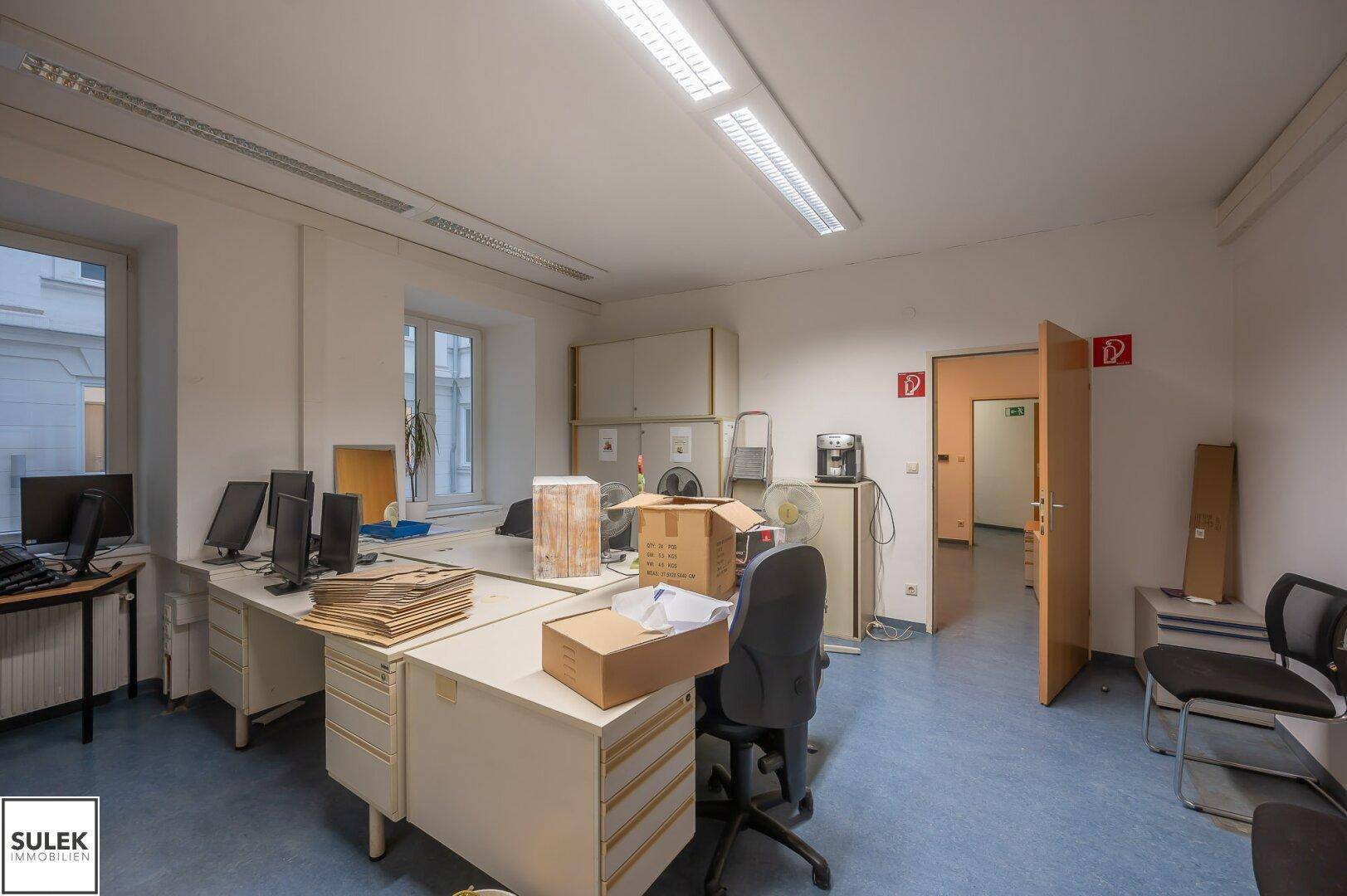 Geräumiges Büro mit mehreren Arbeitsplätzen, Aktenschränken und großen Fenstern für viel Tageslicht.